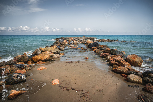Beach on the Italian Riviera with sun, sea and stones in the sea water. Rough Sea and Foamy Waves on Shore at Mediterranean Coast in Sunrise