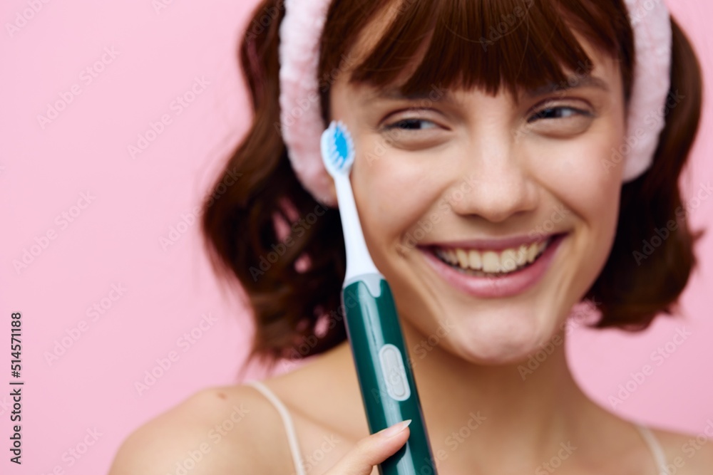 Horizontal studio shot.Close up. A young woman with white skin, a beautiful smile and dark beautiful hair stands on a pink background with a beautiful bandage on her head with a toothbrush. Horizontal studio shot.Close up. A young woman with white skin, a beautiful smile and dark beautiful hair stands on a pink background with a beautiful bandage on her head with a toothbrush.