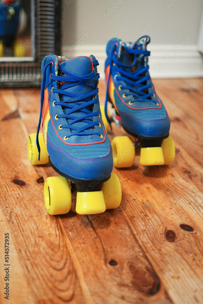 Closeup shot of blue vintage quad roller skates with yellow wheels on wooden floor