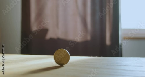 Yellow coin rotates across the wooden surface of the table, casting a shadow. The concept of the circulation of money, savings, bankruptcy. Ukrainian currency, 50 kopecks.
