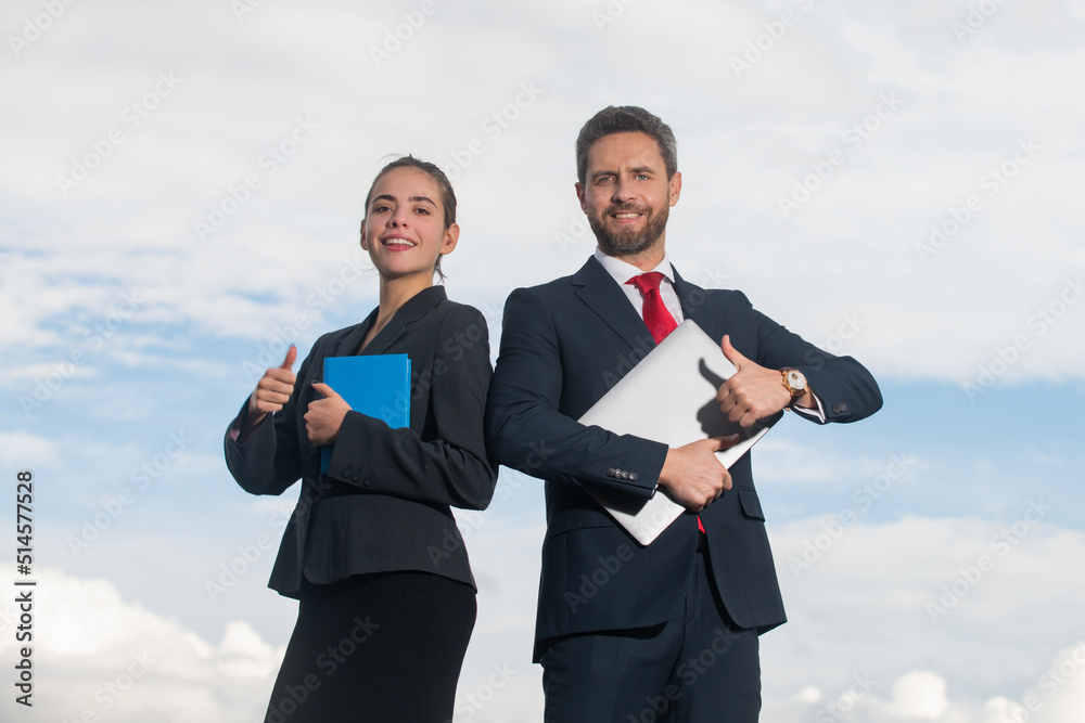 Portrait of business couple in suit with thumbs up. Two young business workers working together with laptop. Secretary and boss. Business people in suit outdoor. Portrait of business couple in suit with thumbs up. Two young business workers working together with laptop. Secretary and boss. Business people in suit outdoor.