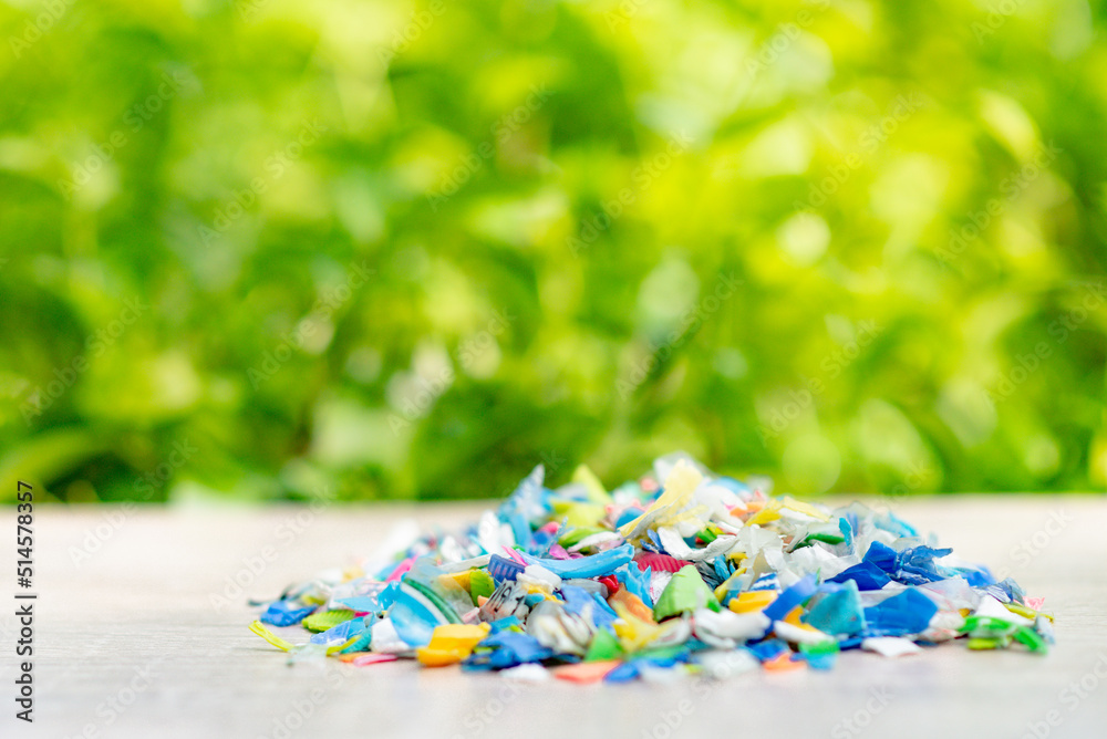 A Pile of PET bottle flakes, Plastic bottle crushed, Small pieces of cut colorful plastic bottles with green blurred background