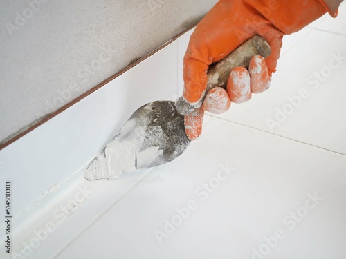 Construction worker in orange gloves is working to grouting between tiles in the bathroom.  photo