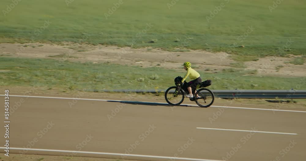 The girl journey on bike on an asphalt winding road. The woman traveler on touring bike with bikepacking bags. The picturesque top view. Live handheld camera follows the model. The girl journey on bike on an asphalt winding road. The woman traveler on touring bike with bikepacking bags. The picturesque top view. Live handheld camera follows the model.