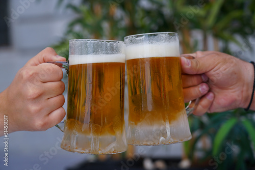 Close-up view of a two glass of beer in hand. Beer glasses clinking at outdoor bar or pub