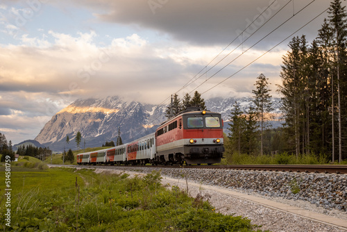 Austrian train rushing past the camera with an electric locomotive of older type and four carriages on early evening..