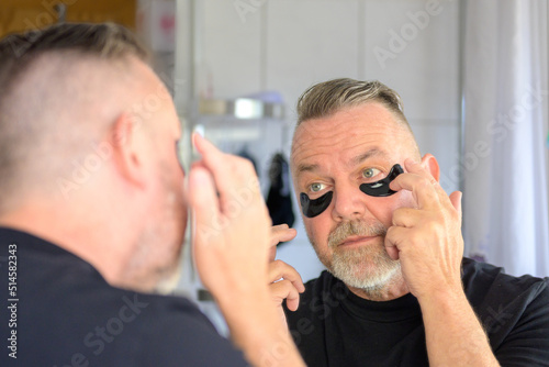 Bearded man applying gel hydration patches to his eyes