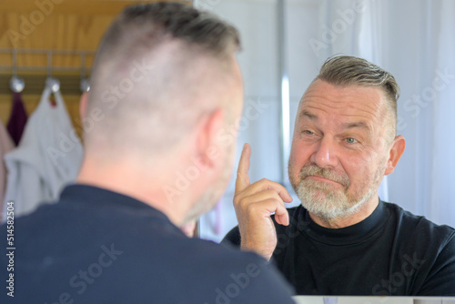 Senior man looking at his reflection with a rueful smile photo