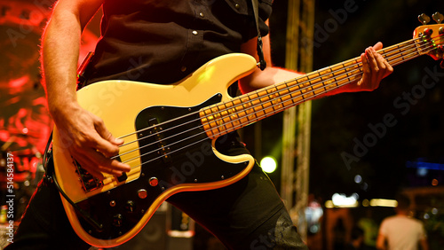 Man playing bass guitar with band on concert, close up. Young musician playing a electric bass guitar on stage. Bass guitar player playing with his fingers and hands on festival. Music instrument.