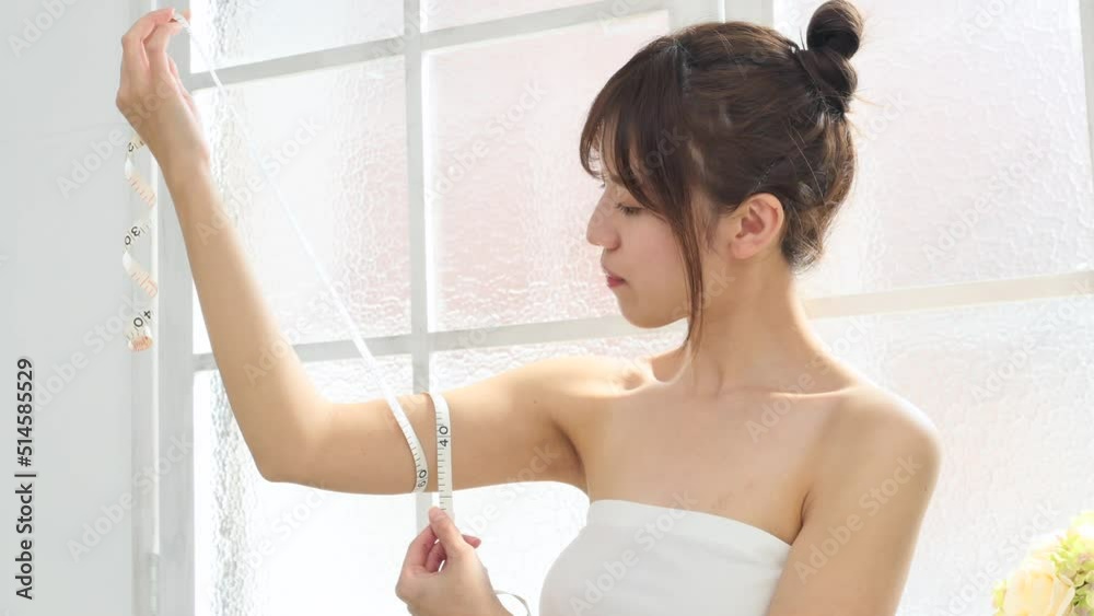 リビングでメジャーで二の腕を測る女性 リビングでメジャーで二の腕を測る女性