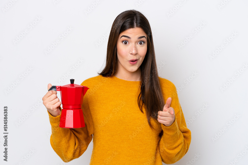 Young Brazilian woman holding coffee pot isolated on white background surprised and pointing front Young Brazilian woman holding coffee pot isolated on white background surprised and pointing front
