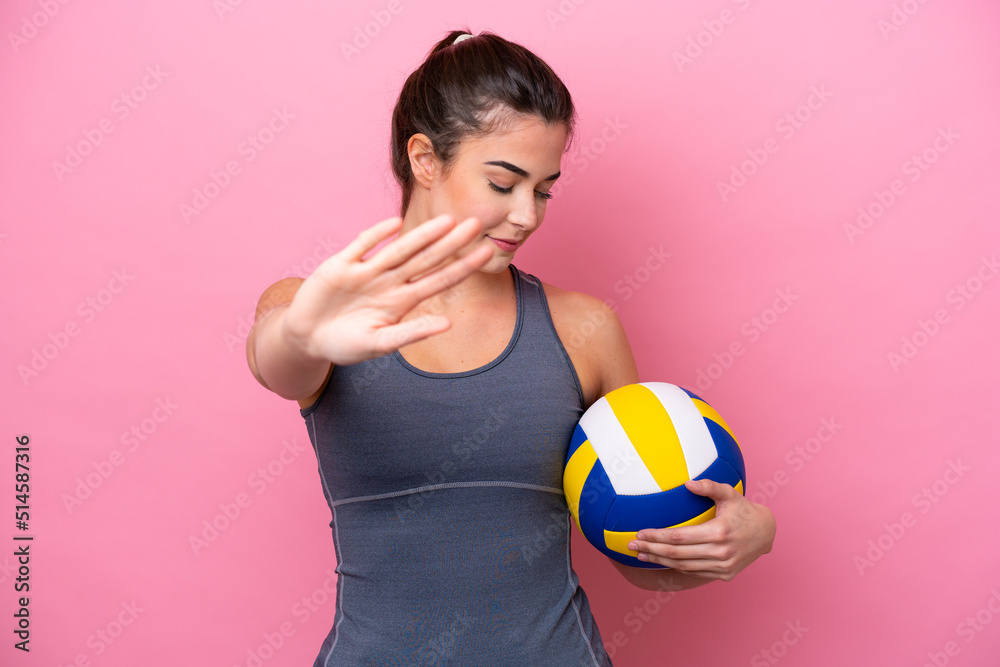 Young Brazilian woman playing volleyball isolated on pink background making stop gesture and disappointed