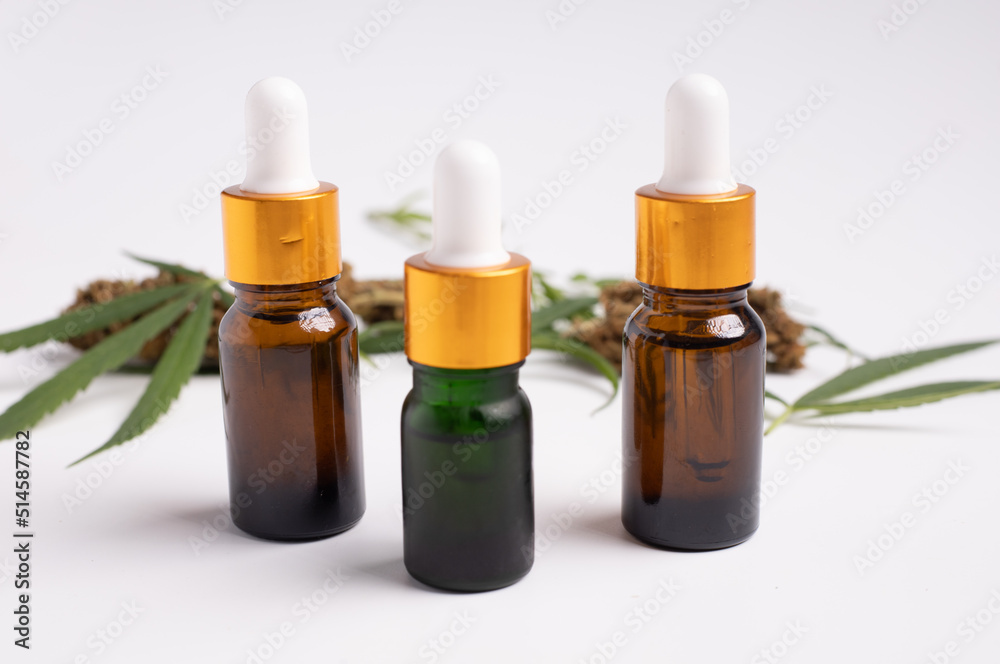 Various glass bottles with CBD oil, THC tincture and hemp leaves on a white background. Various glass bottles with CBD oil, THC tincture and hemp leaves on a white background.