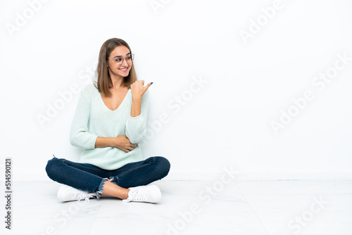 Young caucasian woman sitting on the floor isolated on white background pointing to the side to present a product