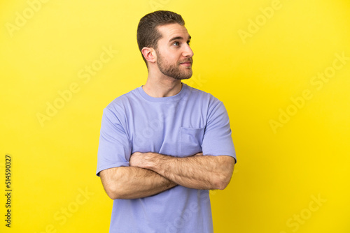 Handsome blonde man over isolated yellow background looking to the side