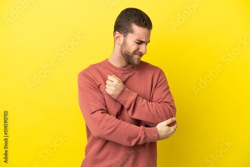 Handsome blonde man over isolated yellow background with pain in elbow