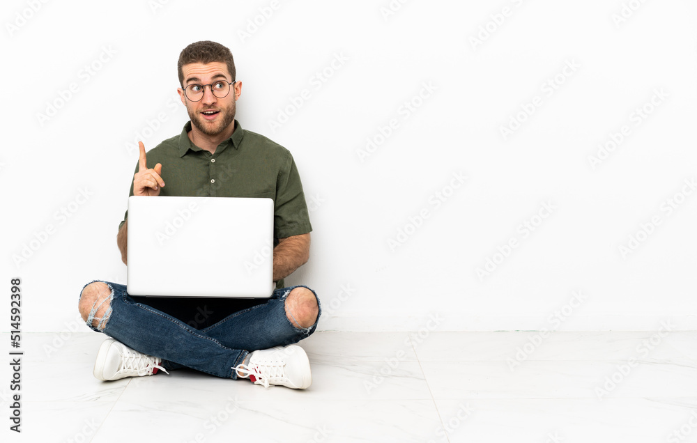Young man sitting on the floor thinking an idea pointing the finger up Young man sitting on the floor thinking an idea pointing the finger up