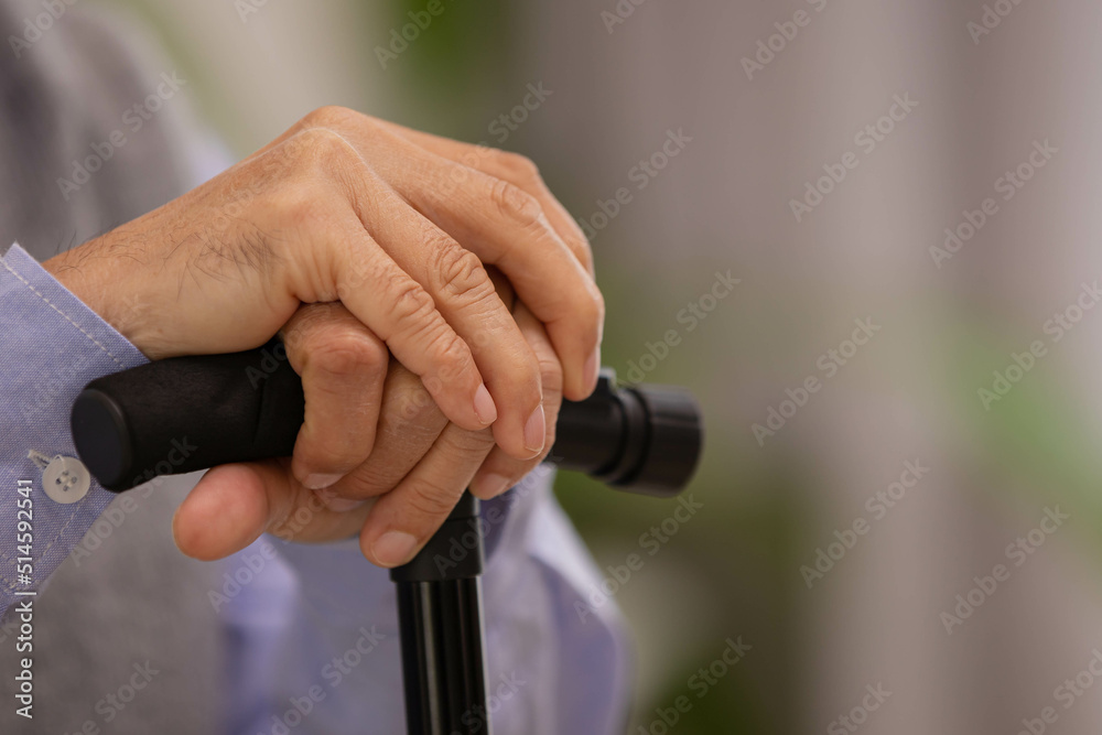 Naklejka premium Close up hand.Asian Elderly man holding walking stick for physiotherapy.Sitting on sofa after walking in morning.