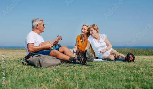 Adult family playing ukulele and singing sitting on a blanket during an excursion outdoors