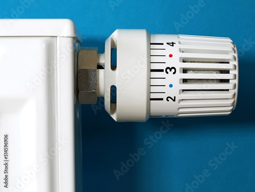 Close-up of a white radiator thermostat on a blue background, conceptual image for rising heating bills