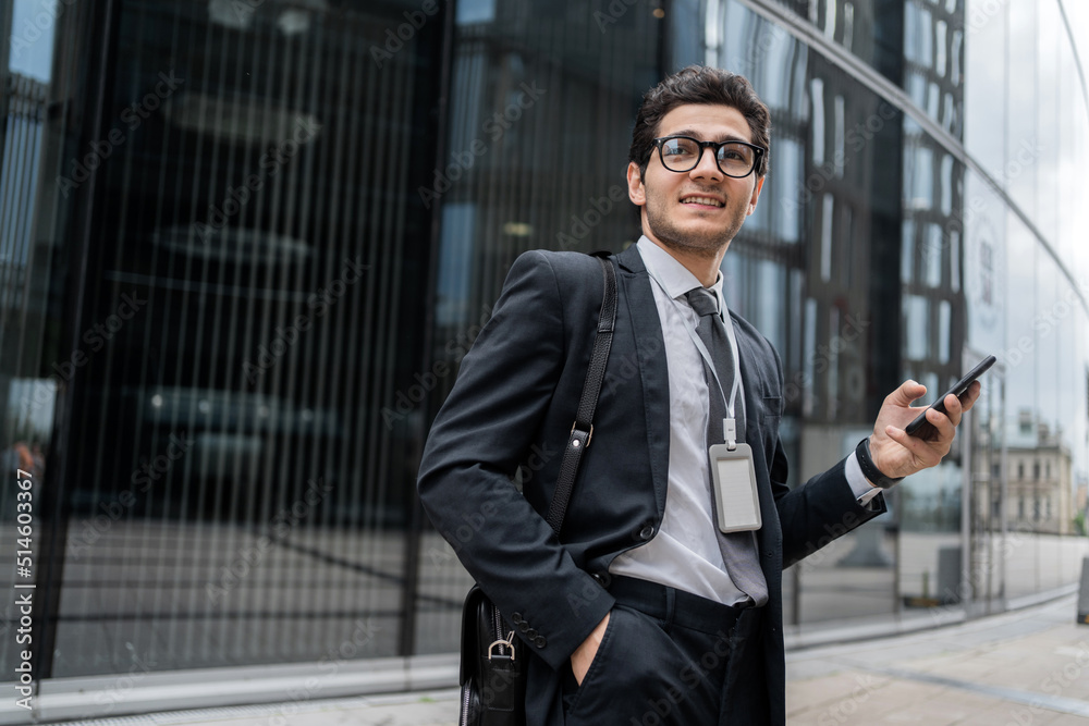 Fototapeta premium A financier uses a phone, writes a message to a colleague, a man with glasses goes to the office to work, in a business suit