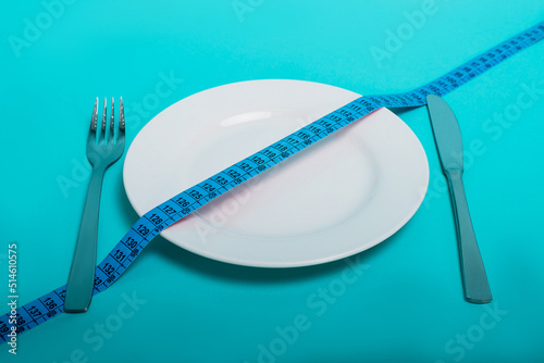 Healthy food, fitness for weight loss. An empty plate with a forkknife measuring tape in centimeters on a blue background from above. Diet menu Obesity. Place for an inscription. Advertising.