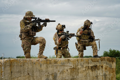 group of military soldier team in uniform with armforce in battle field standing on concrete bunker firing machine gun one of team alert cover
 photo