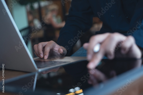 Man working on laptop computer and using digital tablet surfing the internet on wooden table at coffee shop
