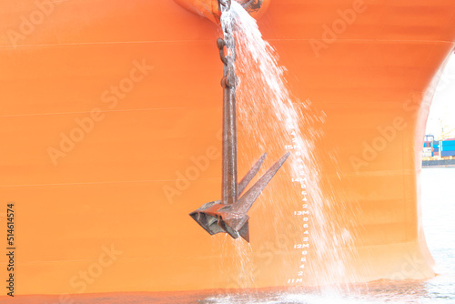 Big rusty anchor on orange with water flowing out of the boat ship in the harbor. At a large port in Thailand. The anchor of a large cargo ship is flowing into the sea to dock for exports and imports.