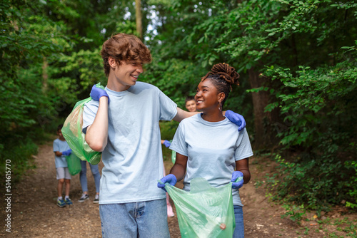Volunteer group cleaning park from rubbish. Young woman and men walking through woods and carrying plastic bags. Outdoor cleaning concept © Graphicroyalty