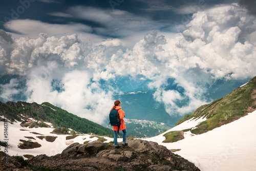 Young woman traveler with backpack standing on the top of the mountain and enjoying the view. Summer landscape of the mountains and sky with clouds. Travel and adventure concept