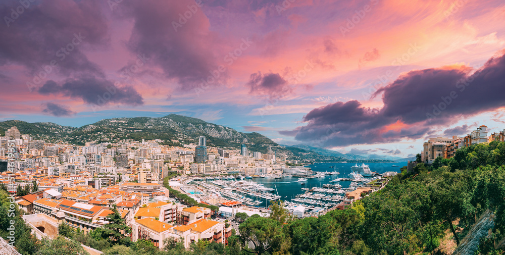 Monaco, Monte Carlo cityscape. Real estate architecture on mountain hill background. Many high-rise buildings in downtown area. Yachts moored at town quay In Sunny Summer Day. Altered Sunset Sky.