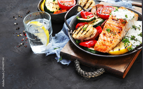 Salmon steak with vegetables and white sauce on dark background.