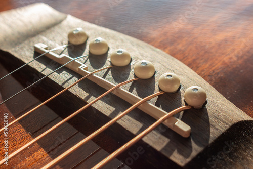 Acoustic guitar bridge with one pins and strings close up with selective shallow focus and blur.