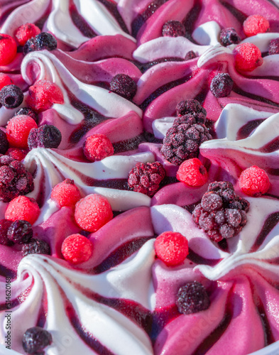 Close up of with pink and white ice cream with forest frozen berries:  black and red currant, blackberry, blueberry, topping sauce. Summer food dessert top. Top view selective shallow focus