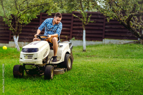 Professional gardener and lawn mower cuts the grass using tractor. Industrial landscaping works