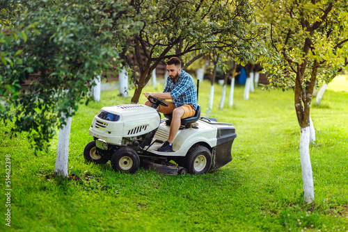 Man using lawn tractor for mowing grass in garden. Landscaping works with professional tools