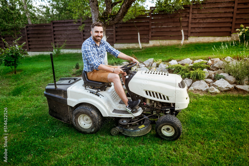 Gardener driving a lawn mower tractor in a garden. . Gardener driving a lawn mower tractor in a garden. .