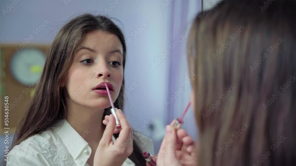 A young girl paints her lips with a special brush in front of a mirror. A young girl paints her lips with a special brush in front of a mirror.