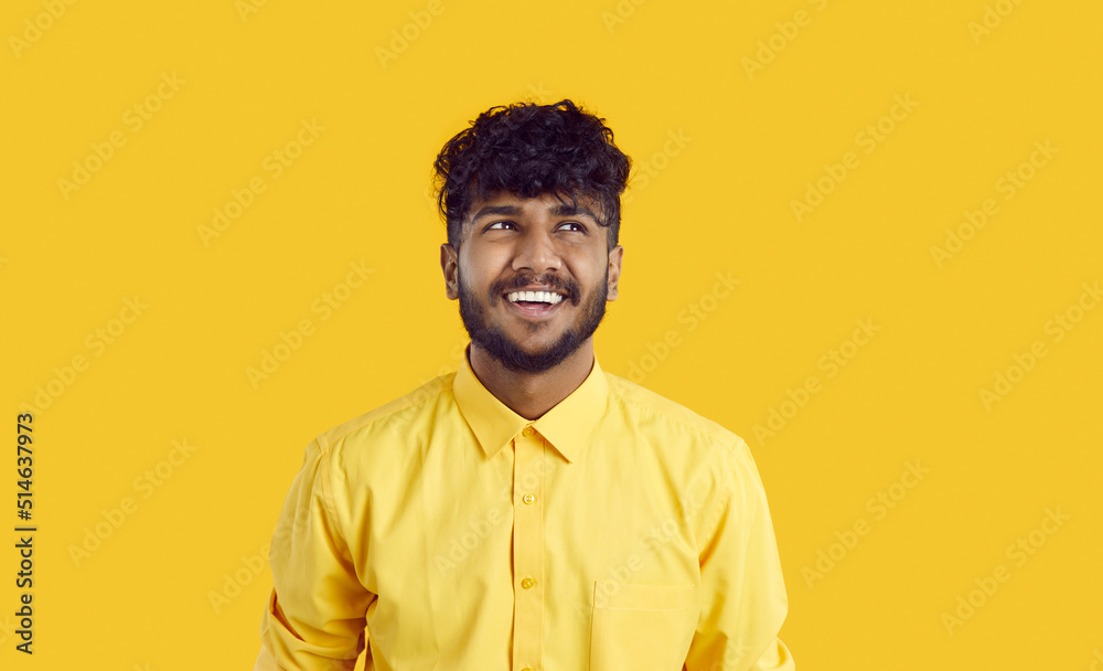 Happy Indian guy with funny expression is thinking about new good opportunities or imagining something nice. Close up of positive funny young man in yellow shirt looking away vivid yellow background Happy Indian guy with funny expression is thinking about new good opportunities or imagining something nice. Close up of positive funny young man in yellow shirt looking away vivid yellow background