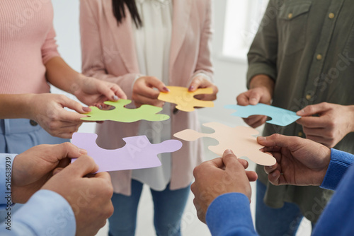 Businesspeople joining puzzle pieces in office. Close up of people's hands holding colored pieces of puzzles symbolizing development and successful completion of tasks. Concept of business cooperation