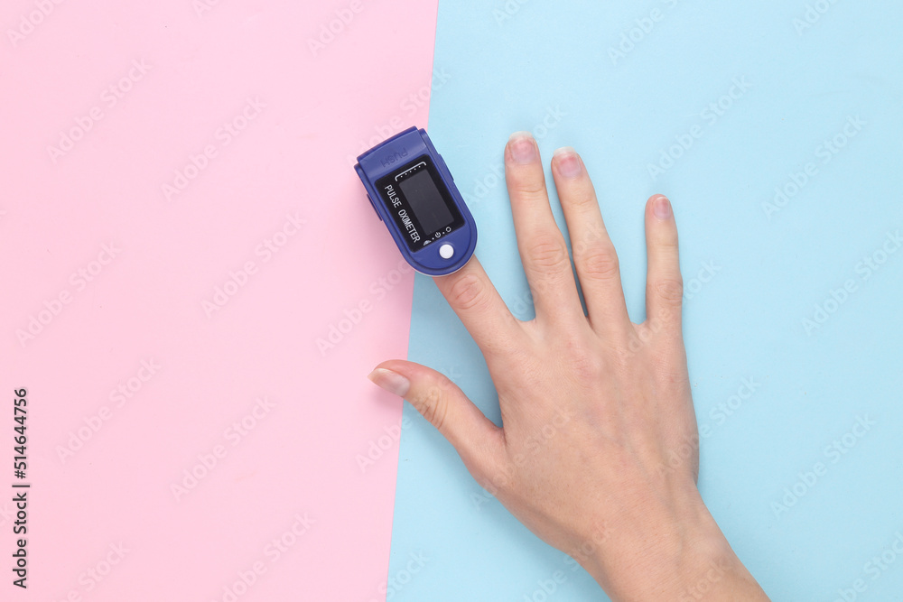 Hand finger with a pulse oximeter on a blue-pink pastel background. Measure the saturation of hemoglobin with oxygen in arterial capillary blood. Hand finger with a pulse oximeter on a blue-pink pastel background. Measure the saturation of hemoglobin with oxygen in arterial capillary blood.