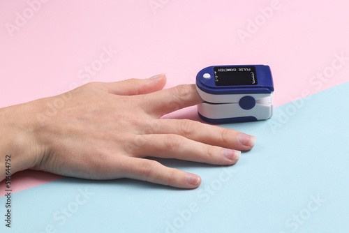 Hand finger with a pulse oximeter on a blue-pink pastel background. Measure the saturation of hemoglobin with oxygen in arterial capillary blood.