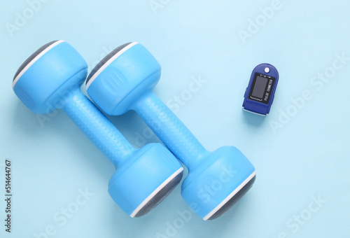 Health care. Healthy lifestyle concept. Dumbbells with a pulse oximeter on a blue background. Top view