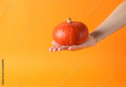 Hand holding pumpkin on orange background