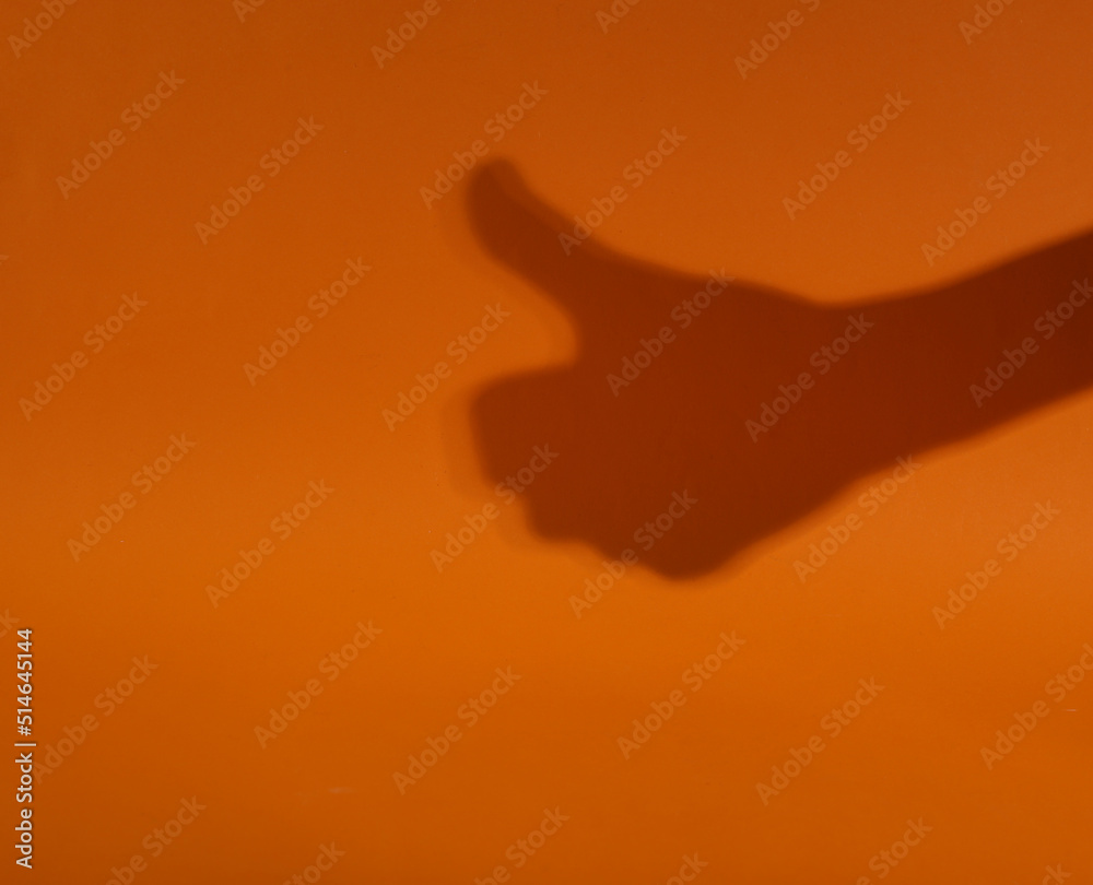 Minimal halloween concept. Hand shadow showing thumb up on orange background