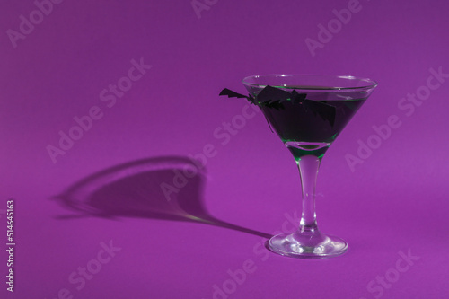 Halloween party. Cocktail with green liquid and bats on purple background