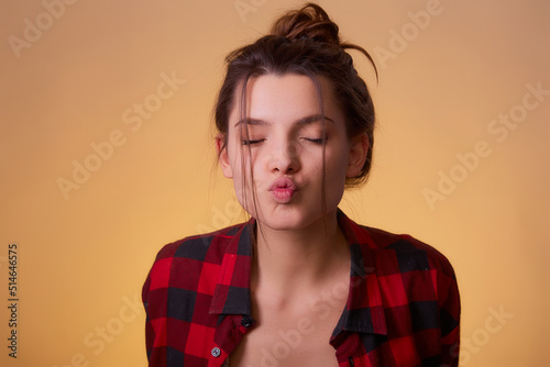 Portrait of funny childish woman send fun air kiss boyfriend valentine day date, celebration wear red n checkered shirt isolated over yellow background