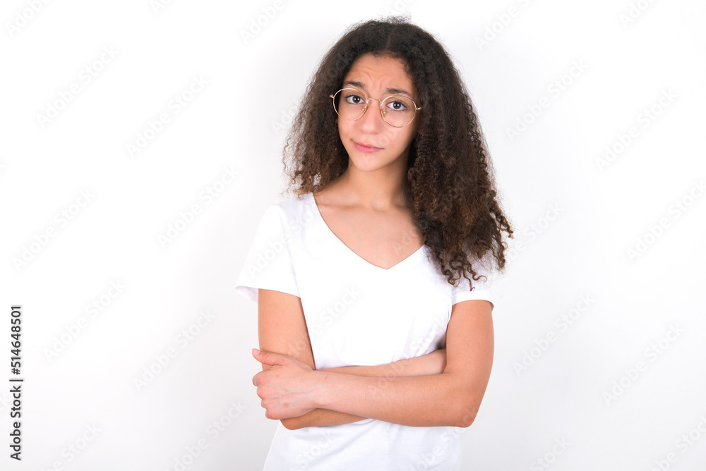 young beautiful girl with afro hairstyle wearing white t-shirt over white wall bitting his mouth and looking worried and scared crossing arms, worry and doubt. young beautiful girl with afro hairstyle wearing white t-shirt over white wall bitting his mouth and looking worried and scared crossing arms, worry and doubt.