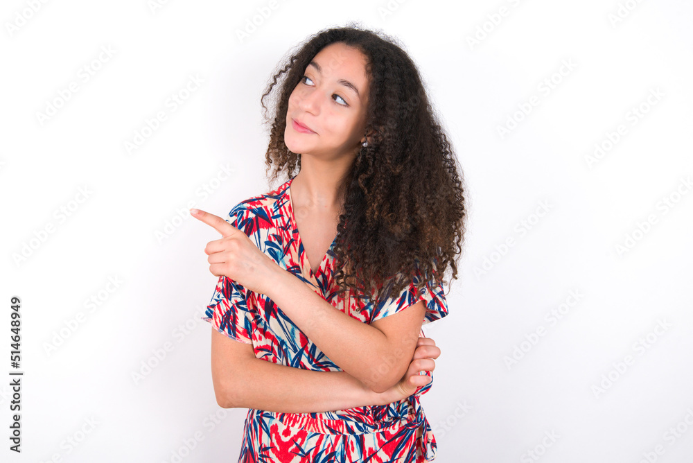 Portrait of young beautiful girl with afro hairstyle wearing flowered dress posing on camera with tricky look, presenting product with index finger. Advertisement concept. Portrait of young beautiful girl with afro hairstyle wearing flowered dress posing on camera with tricky look, presenting product with index finger. Advertisement concept.